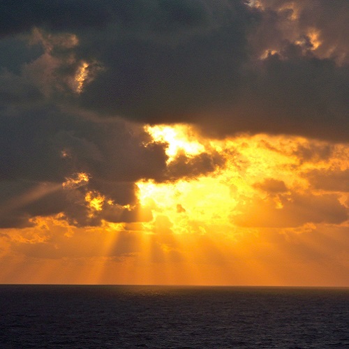 image of a sun setting through clouds over the ocean
