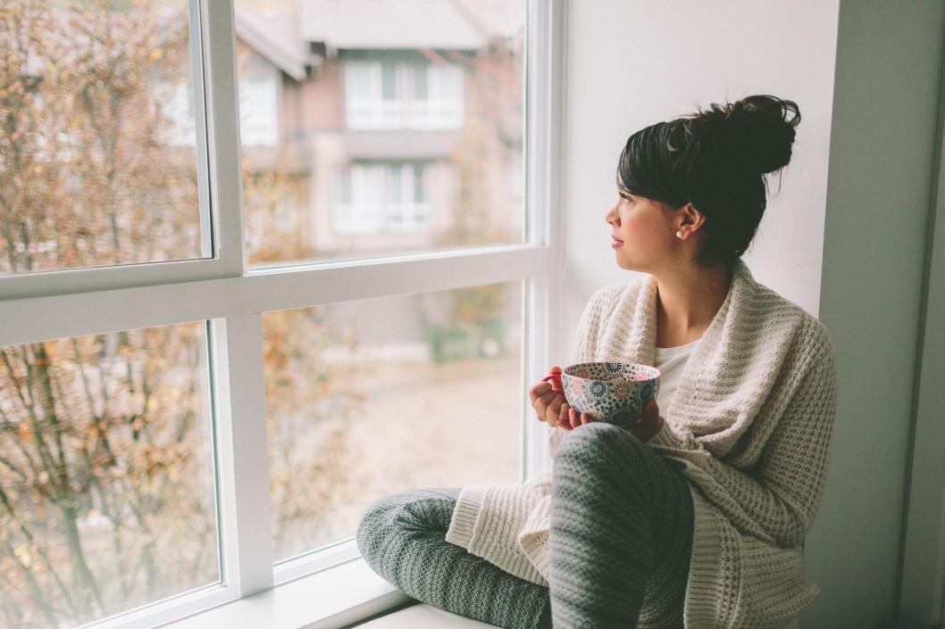 Young woman drinking tea while looking out a large window
