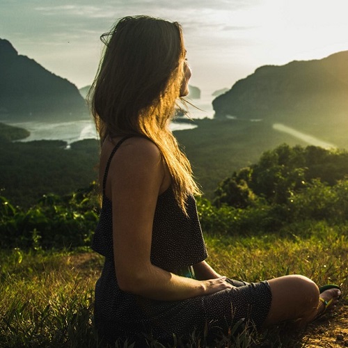 image of a young woman sitting on a hill watching the sunrise over the ocean