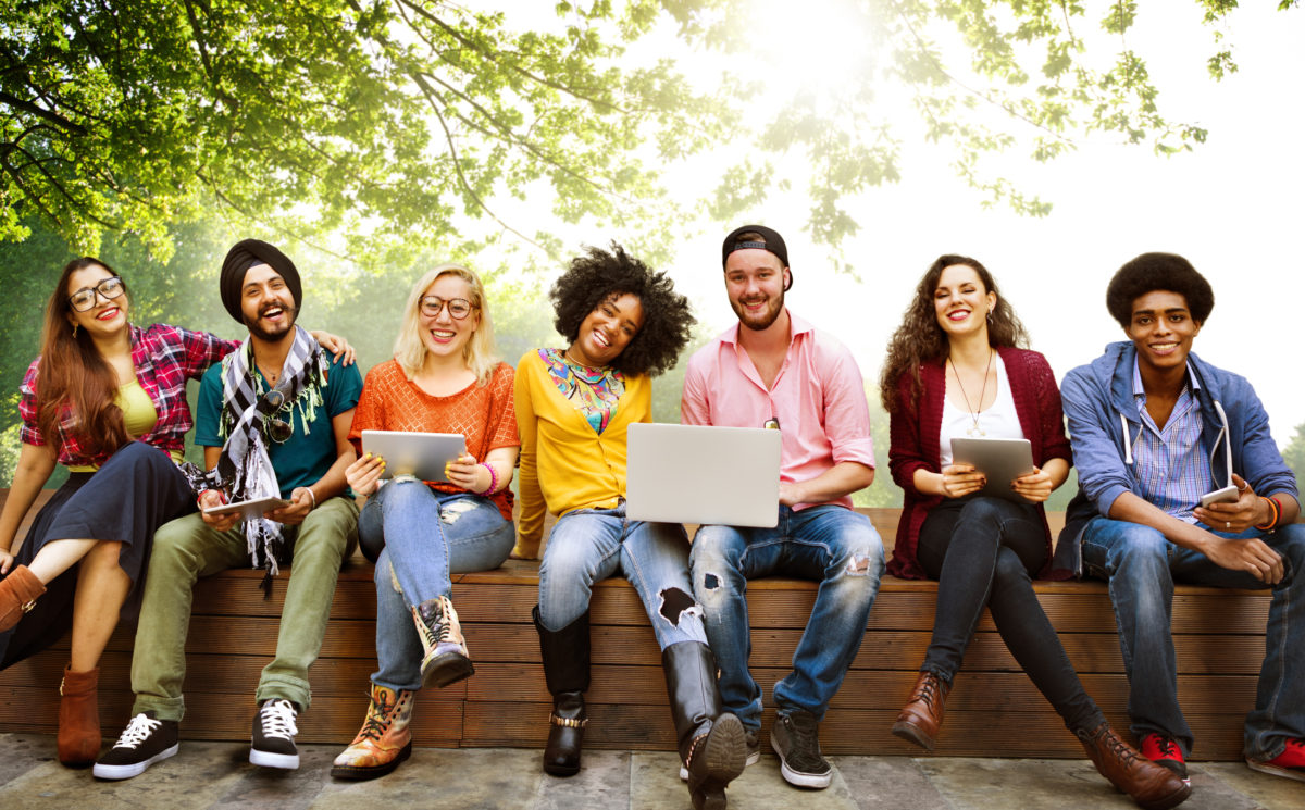 image of a group of young adults sitting on a bench holding laptops and smiling