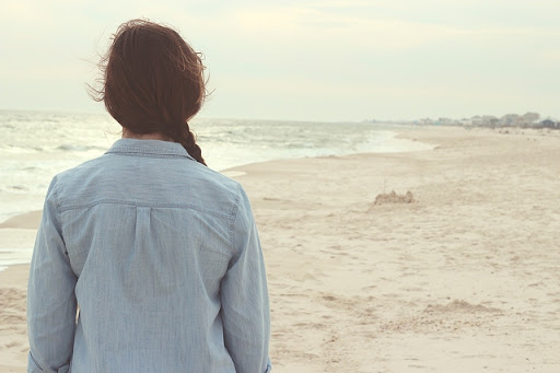 image of a young woman standing on a beach staring at a sand castle