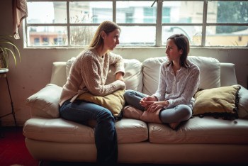 image of two young women sitting on a couch having a serious conversation