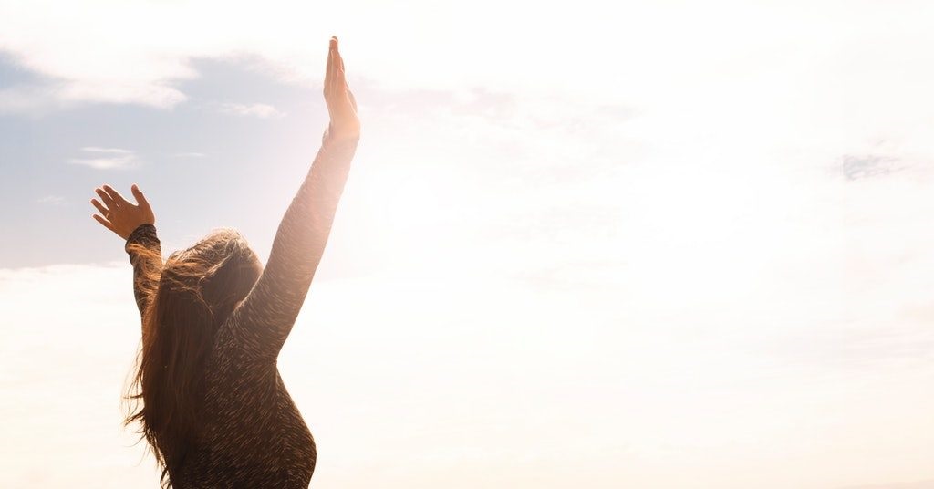 image of a young woman raising her hands in sunlight