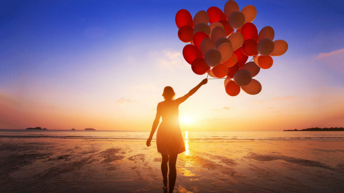 image of a young woman on the beach holding a batch of balloons at sunset