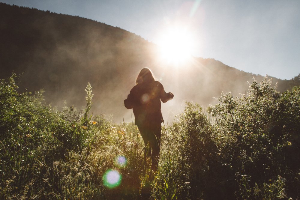 image of a young woman running up a hill into bright sunlight