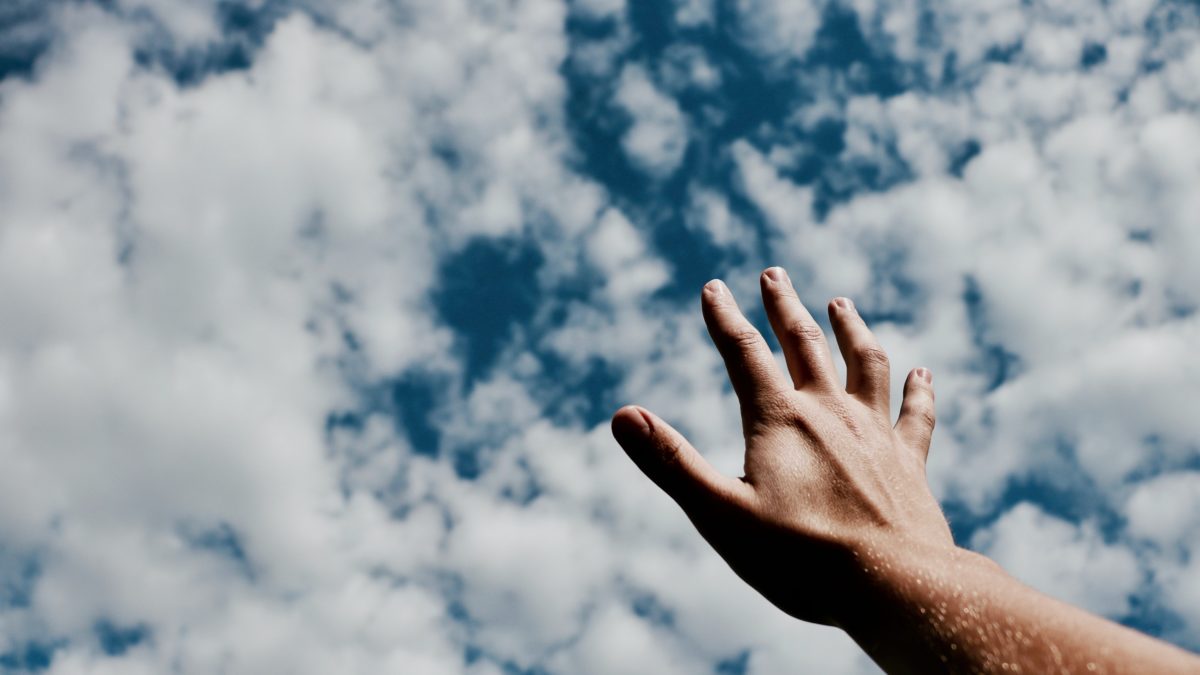 hand reaching up toward cloudy sky