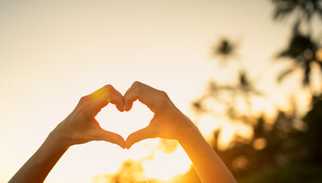 person creating a heart with their hands in front of blurred background