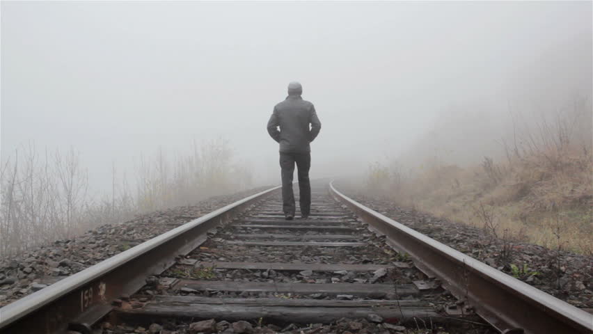 man walking on train tracks into fog
