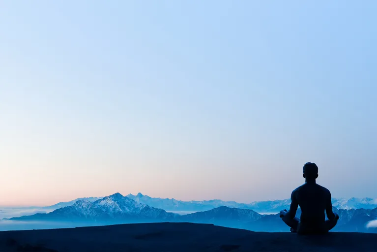 person sitting mediating in front of blue sky and mountains