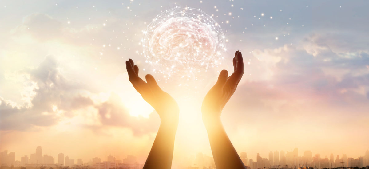 raised hands cupping illustration of a brain in front of sunset