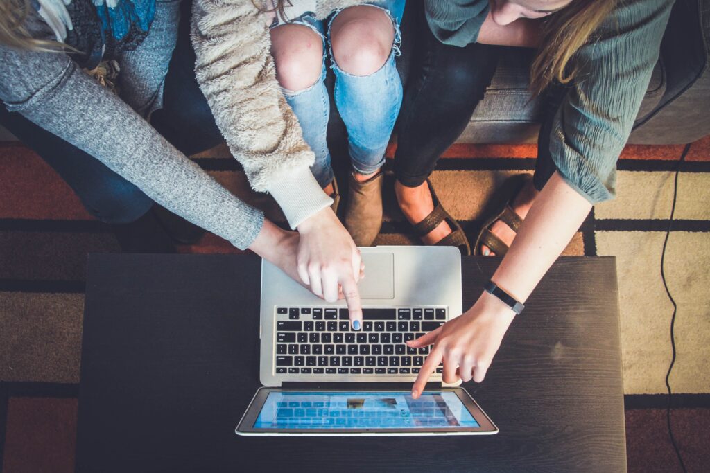 three individuals sitting on couch pointing to laptop screen