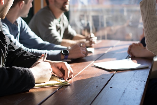 people sitting around a sunlit table, only their hands and parts of their faces are visible