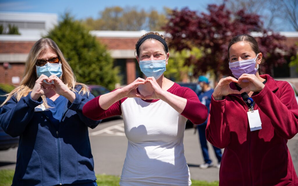 three women wearing masks standing in a line, making heart symbols