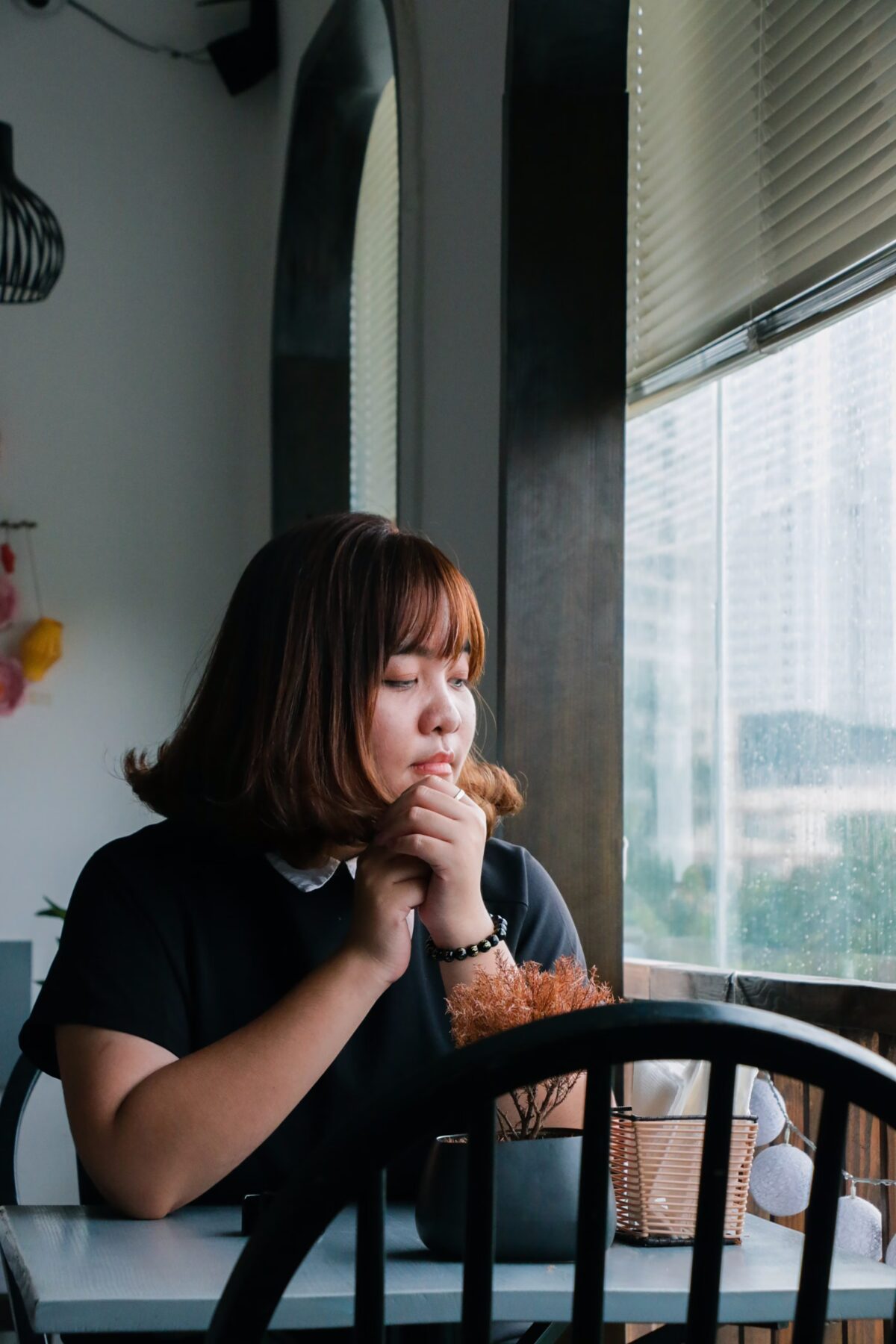 woman looking pensively out the window while sitting at a table