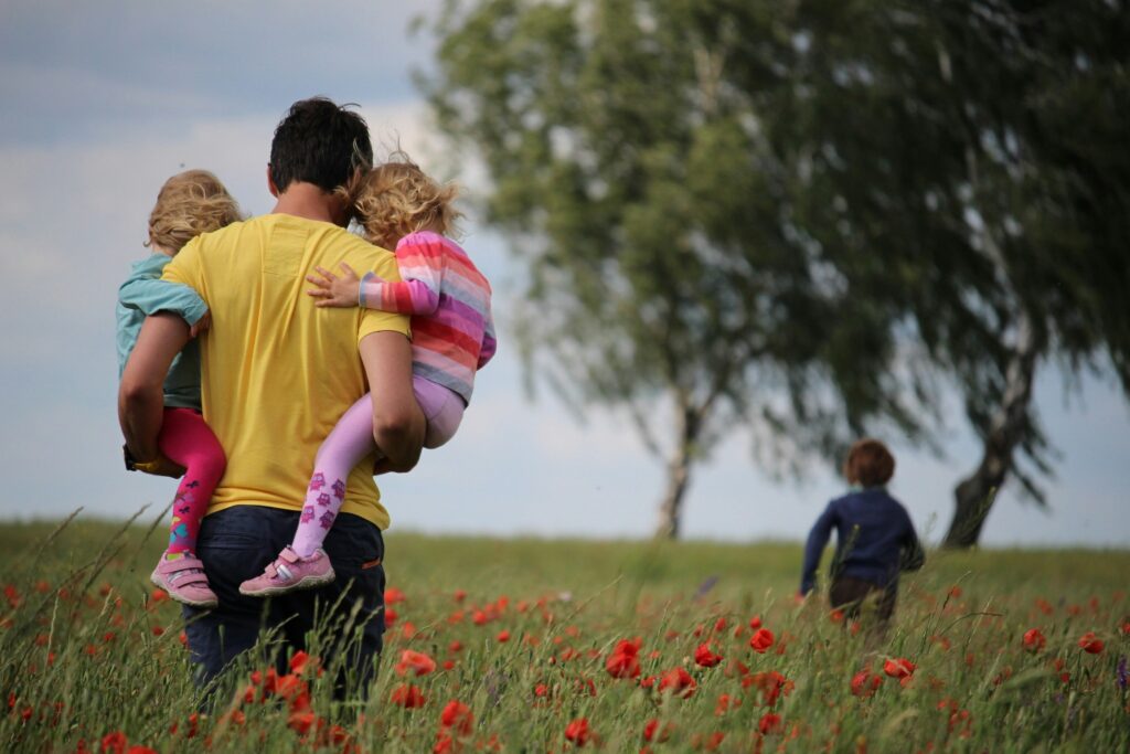 Father carrying two children in a field and walking towards another child