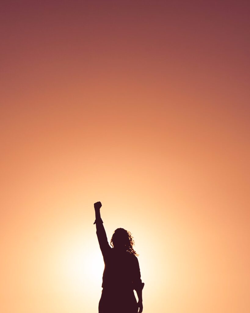 woman standing against a sunlit background holding her fist up into the sky