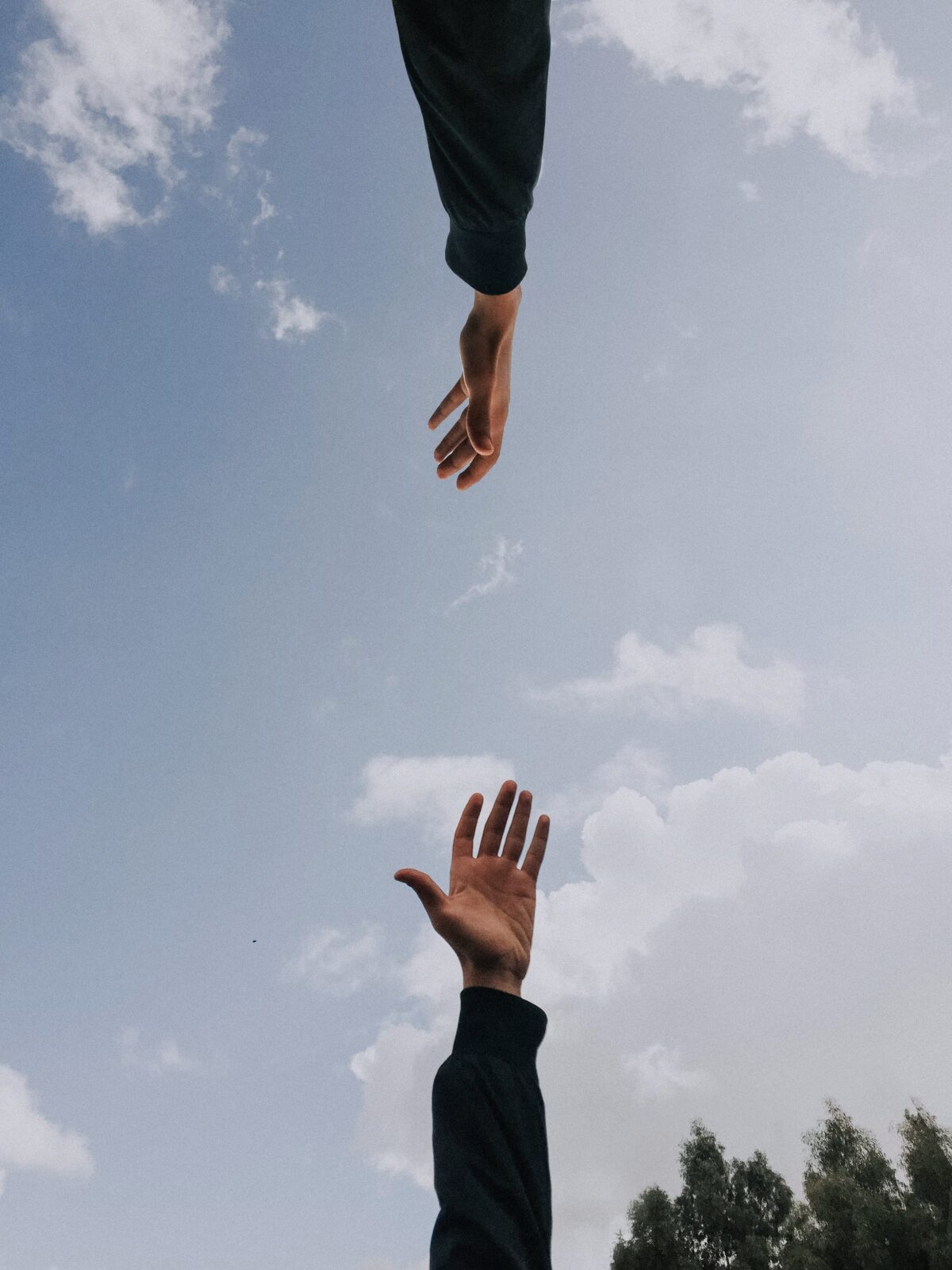 two hands reaching towards eachother from below, sky in the background