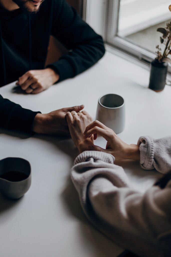 two people holding hands across a table with a cup of coffee between them