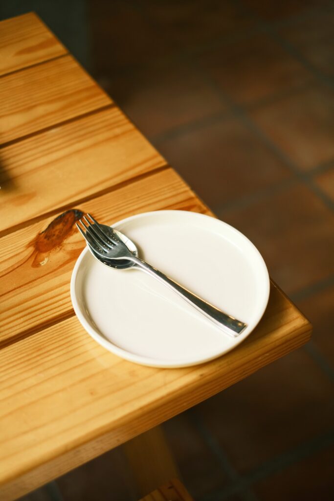 a  white plate on the corner of a table with a fork in the middle, no food is present