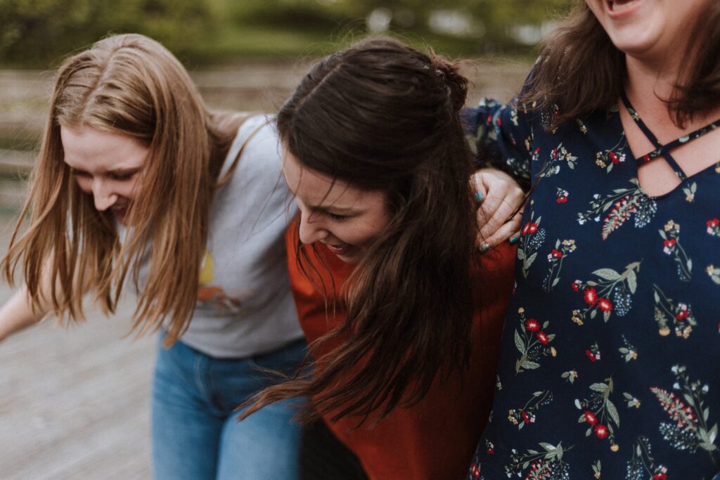 a group of three women, linked arms, bending over laughing