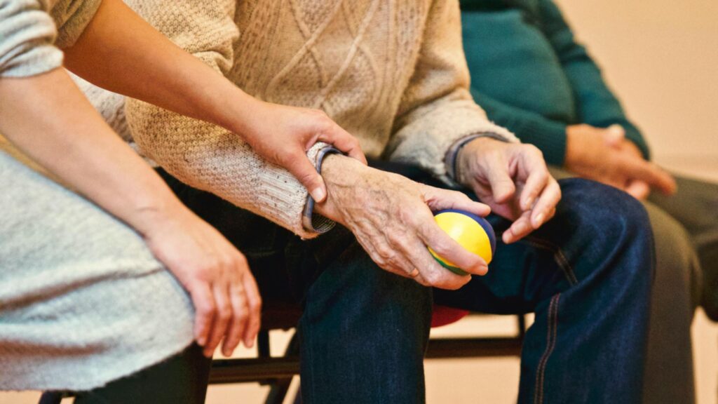 older adult holds a stress ball while sitting in a chair