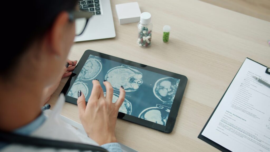 A medical professional look at a touchpad screen on which there is a brainscan image