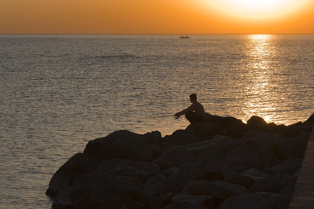 a man sits on a very rocky beach side near sunset