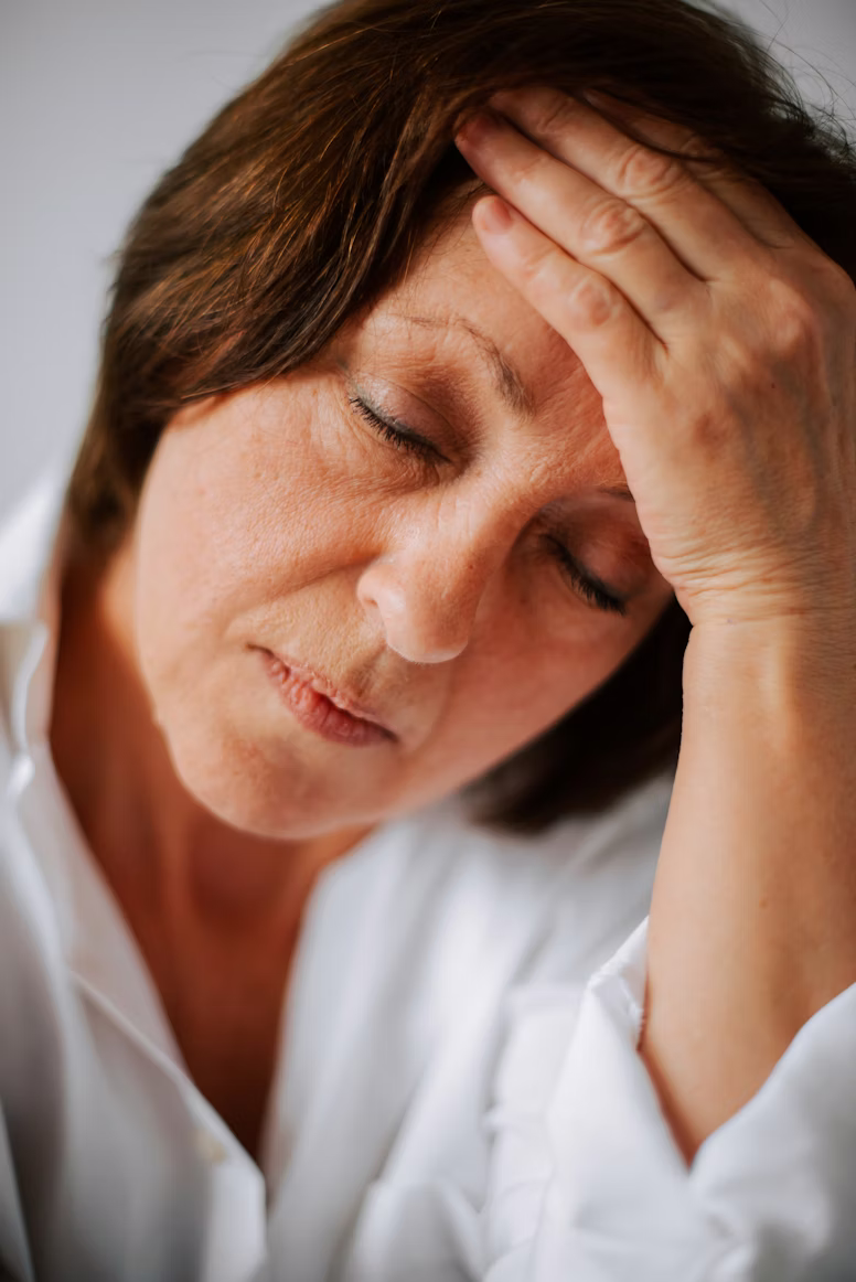 A woman leans her forehead into her hand with her eyes closed