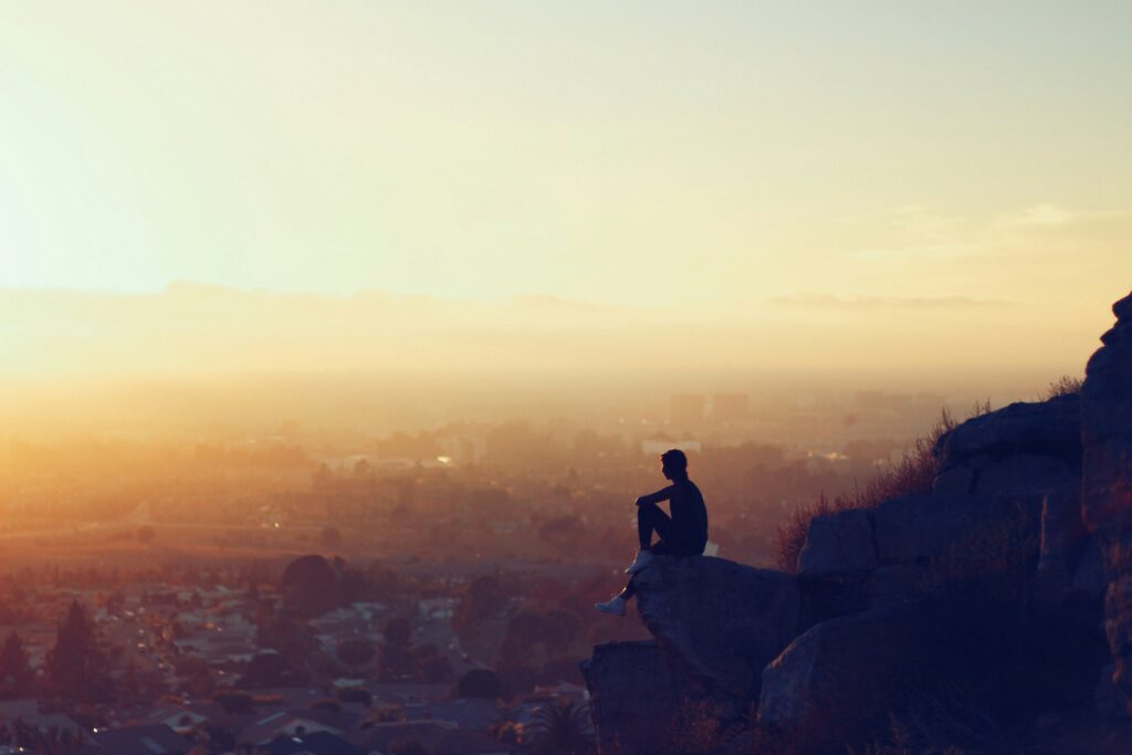 A person sits on a ledge outside looking out at the horizon