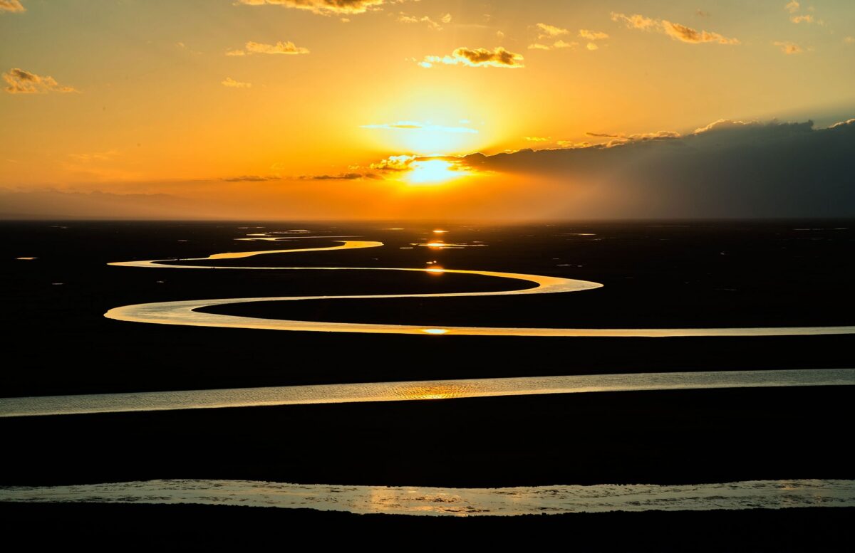 The sun sets over the silhouette of a winding river