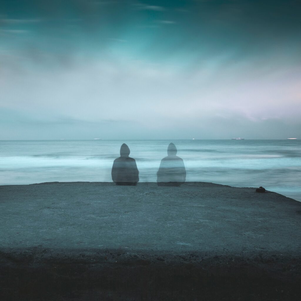 Two people are faded out as shadows in front of a lakeshore.