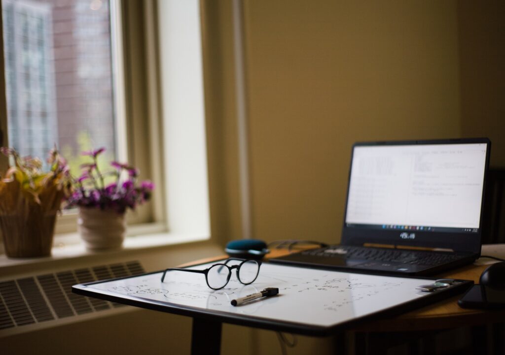 A laptop, glasses, white board, and marker sit on a table