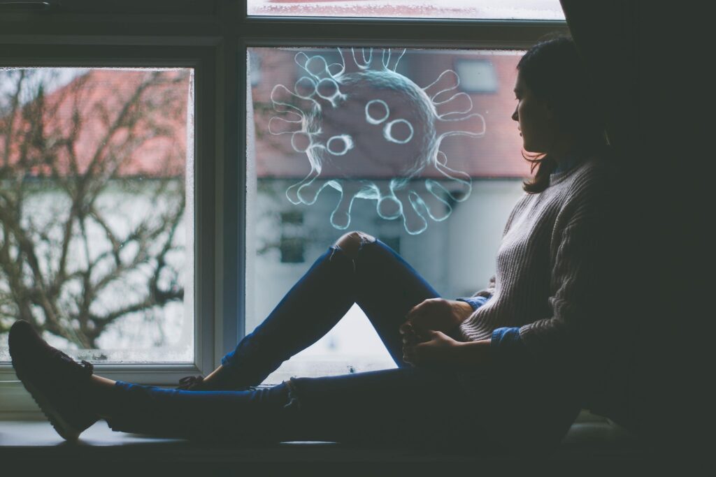 A woman sits looking out a window where a softly outlined bacteria-like unknown substance is present