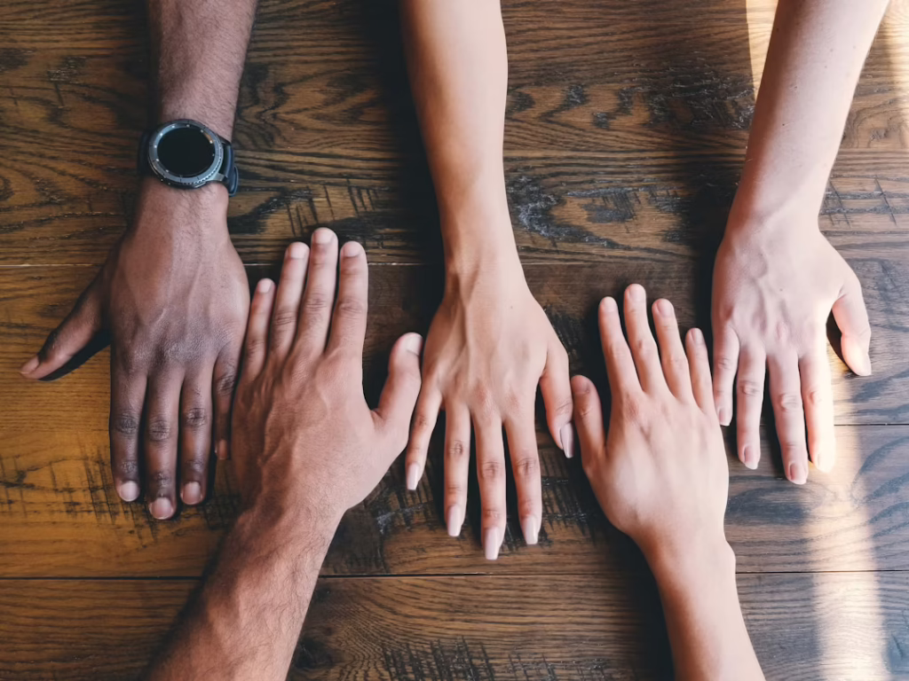 Five hands of different skin tones are outstretched on a wooden surface